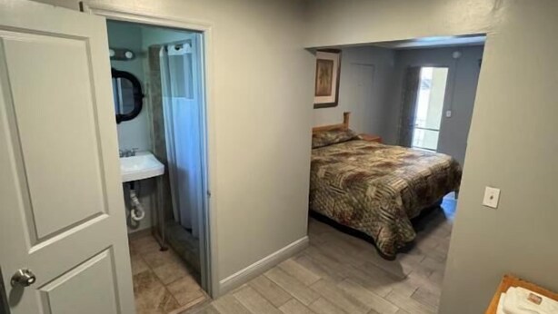 Quarto com cama, banheiro com chuveiro e porta que dá para outro cômodo.
