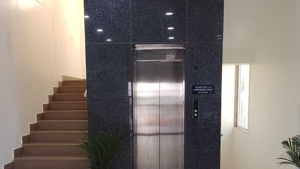 Un ascenseur moderne dans un hall d’entrée agrémenté d’un escalier, de plantes en pot et d’un panneau indiquant que l’ascenseur est réservé à un maximum de quatre personnes.