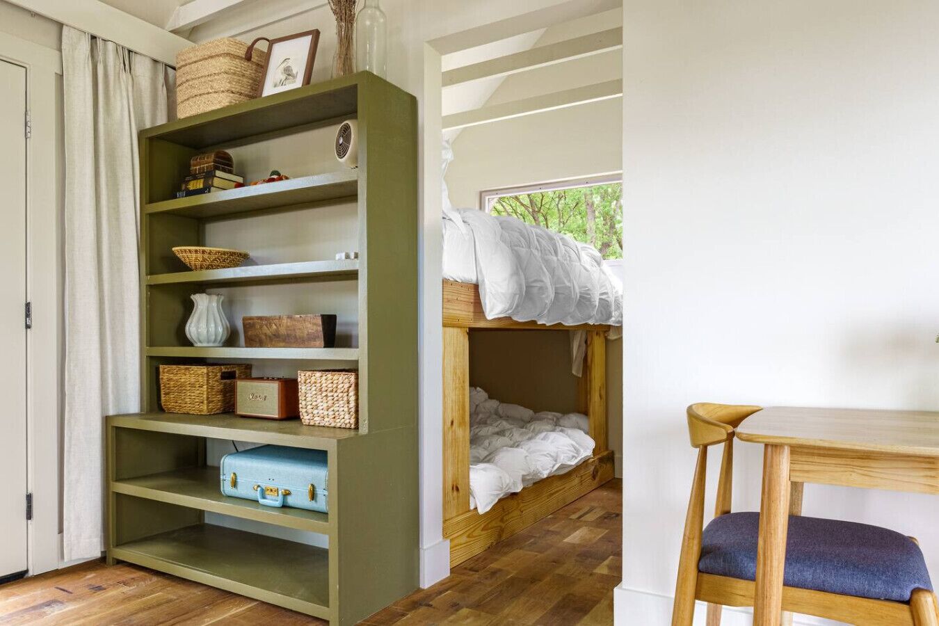 Ein Zimmer mit Etagenbett, einem Holztisch und einem Bücherregal mit Körben und einem Vintage-Radio.