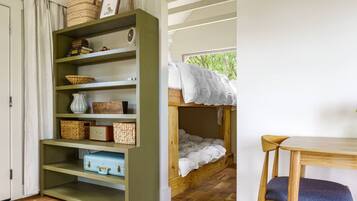 Ein Zimmer mit Etagenbett, einem Holztisch und einem Bücherregal mit Körben und einem Vintage-Radio.