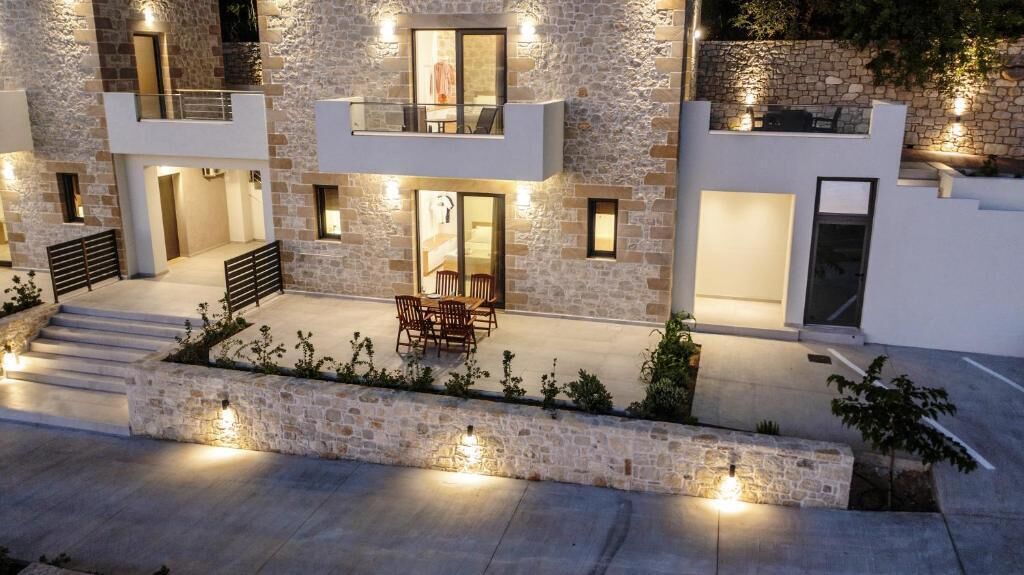 Een modern gebouw met twee verdiepingen, een gevel van natuursteen, terras en verlichte ramen.
