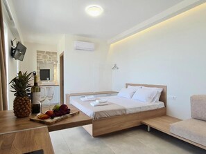 A modern bedroom with a wooden bed, a small table with fruit and wine, and a TV on the wall.