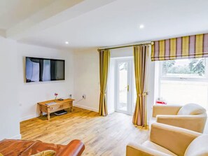 Ein Zimmer mit Holzboden, Schreibtisch, Stuhl, Fernseher und einem Fenster mit Vorhängen.