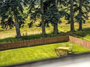 Un espace extérieur clos, avec une table et des chaises en bois, entouré d’arbres et d’herbe.