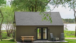A small cabin with a picnic table and chairs, a door, and a small porch area. - Cozy & Family-Friendly Lake Oasis: Ofuro Tub, King Bed, Bunks & Workspace! (Jewett)