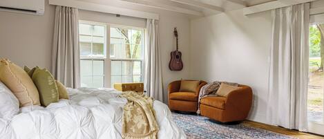 A bedroom with a large bed, a wooden floor, a patterned rug, a guitar, and a suitcase.