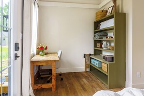 Ein Zimmer mit einem Holztisch, einem Stuhl, einem Bücherregal und einem fenster mit Vorhängen.