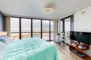 Ein Zimmer mit einem großen Bett, einem Fernseher und Blick auf den Strand.