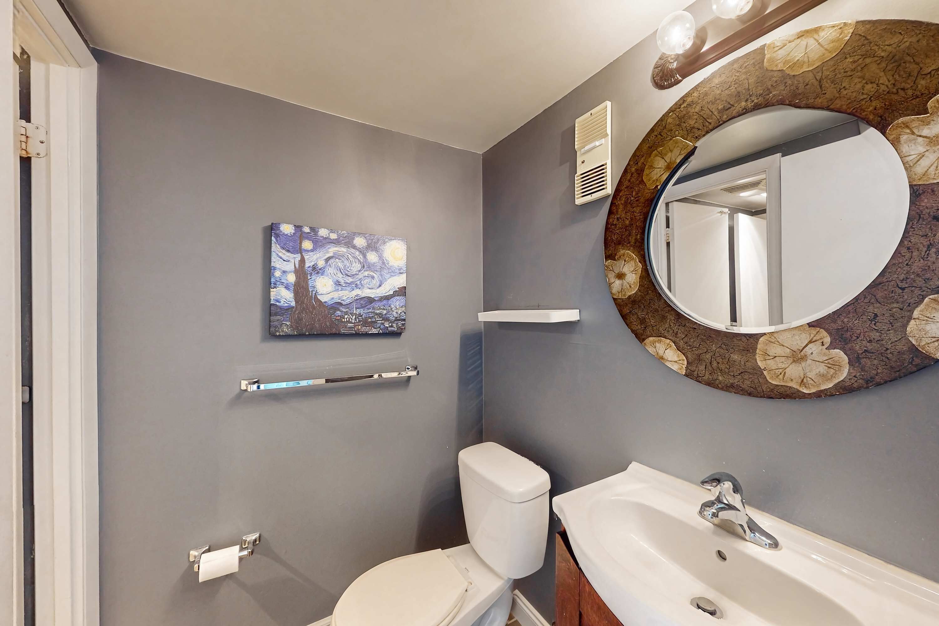 Une salle de bain avec des toilettes, un lavabo, un miroir et un tableau accroché au mur.