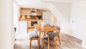 Een moderne keuken met houten kastjes, een eettafel met stoelen, en een trap die naar een ander niveau leidt.