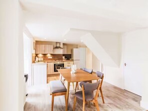 Eine moderne Küche mit Holzschränken, einem Esstisch mit Stühlen und einer Treppe, die eine weitere Ebene hinaufführt.
