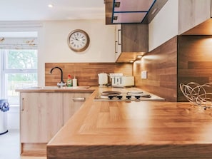Eine moderne Küche mit Holzausstattung, einem Einbauherd, einem Spülbecken und einer Wanduhr.
