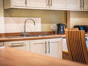 Eine Küche mit Edelstahl-Spüle, Holz Arbeitsplatte, weißen Schränken und einer Kaffeemaschine.