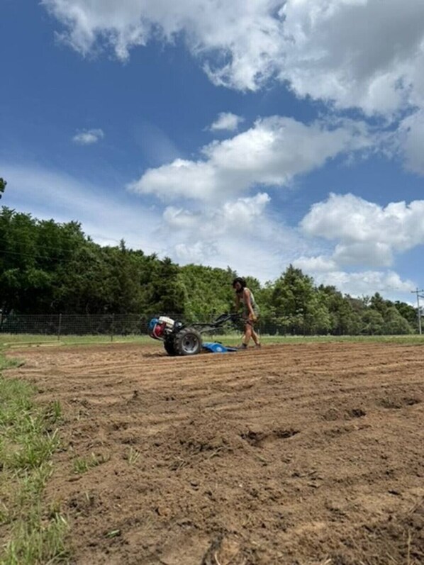 Una persona operando un tractor en un campo con una valla y árboles al fondo.