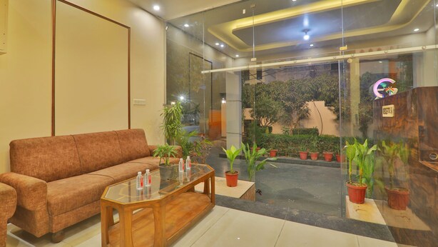 A reception area with a sofa, a glass coffee table, potted plants, and a glass wall with a view of greenery. - HOTEL O BLUE DIAMOND (Lucknow)
