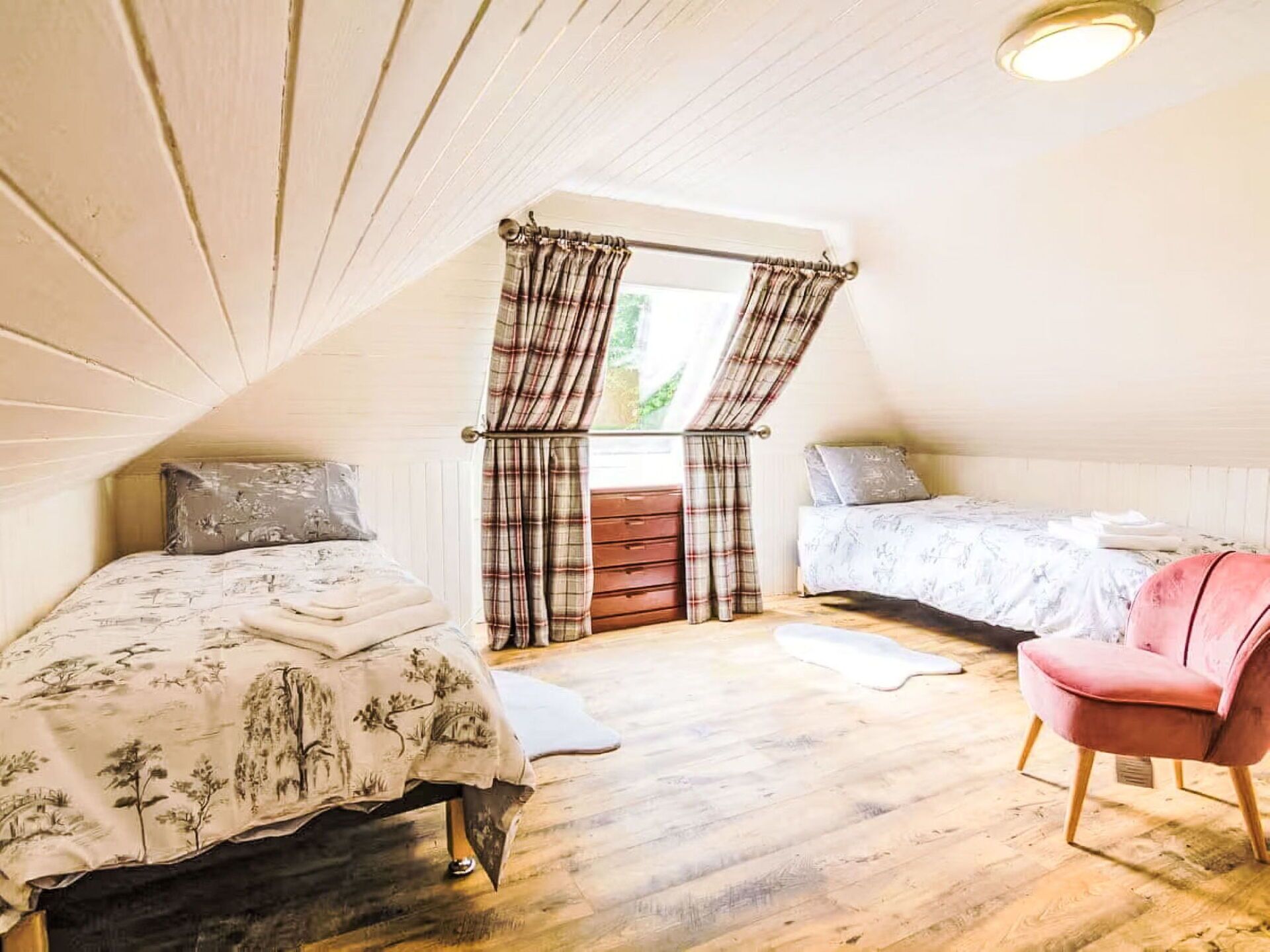 A cozy attic bedroom with two beds, a red chair, and a wooden floor.
