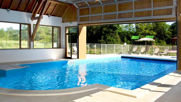 An indoor swimming pool with clear views of the outdoors, a covered roof, and a fenced area with lounge chairs. - Duplex Maisonette in the Heart of Dordogne (Bergerac)