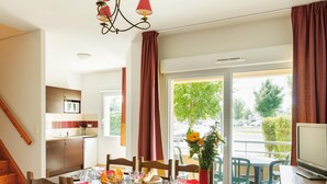 A dining area with a table set for four, a kitchen in the background, and a balcony with a view of the outdoors. - Duplex Maisonette in the Heart of Dordogne (Bergerac)