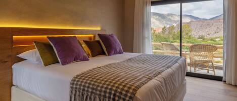 Un dormitorio con una cama grande, vistas a las montañas y un balcón con mobiliario de mimbre.
