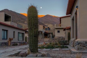 Edificio de estilo desértico con un camino de piedra, cactus y montañas al fondo.