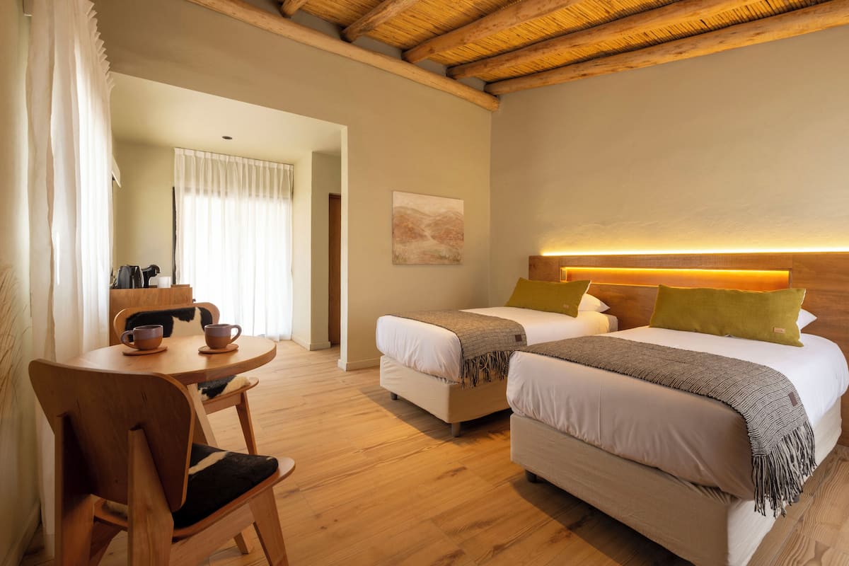 Un dormitorio con dos camas, una mesa de madera con sillas y un cuadro en la pared.