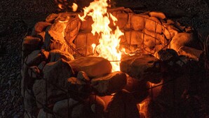 Un hogar de piedra rodeado de rocas, con llamas, en un entorno exterior nocturno.