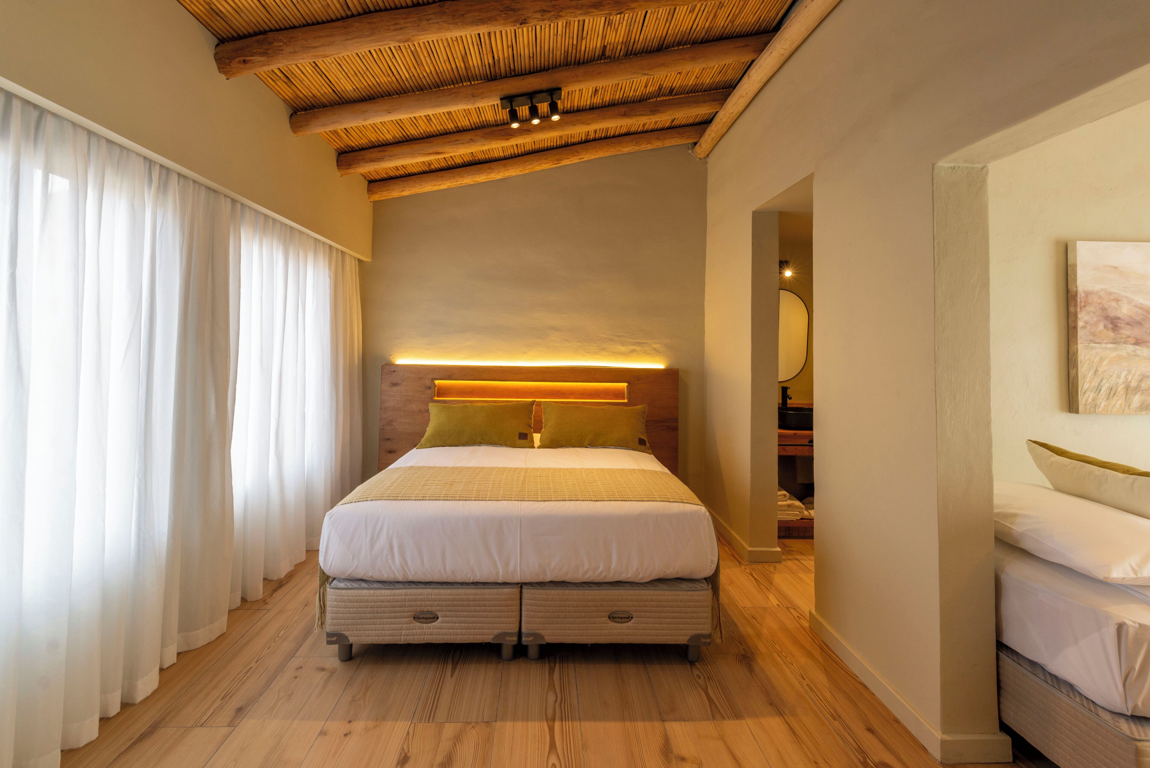 Een slaapkamer met een bed, houten vloeren, een plafond met zichtbare balken, een nachtkastje en een bedtafel.