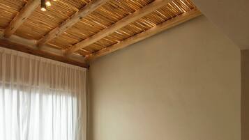Een slaapkamer met een houten plafond, een bed met kussens, een stoel en een klein tafeltje.