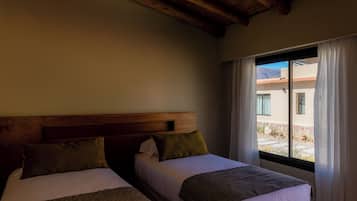 Two beds with wooden headboards, a window with curtains, and a view of a building outside.