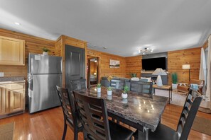 A modern kitchen with a stainless steel refrigerator, wooden cabinets, a marble dining table, and a cozy seating area with a fireplace. - Lake Views! Cozy Cabin, Hot Tub, Kayaks, and Pool! (Forsyth)