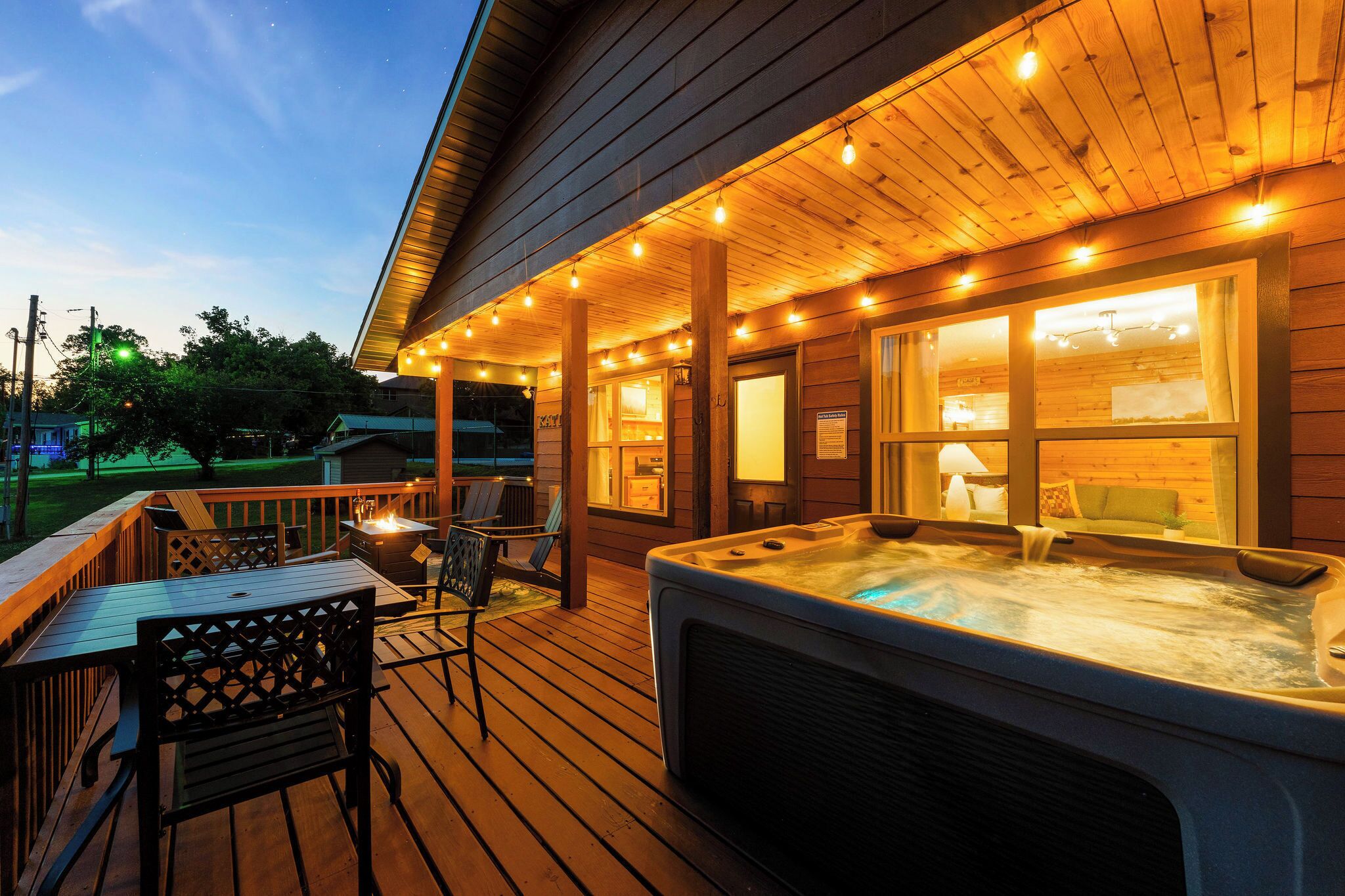 A wooden deck with a hot tub, outdoor seating, and string lights.
