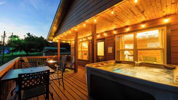 A wooden deck with a hot tub, outdoor seating, and string lights.