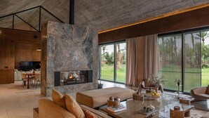 Una sala moderna con chimenea de piedra, asientos cómodos, zona de comedor y ventanas amplias con vistas a vegetación.