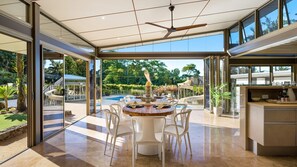 A modern dining area with a round table, white chairs, and a view of a swimming pool and greenery. - Glenbrook House and Studio (Ewingsdale)