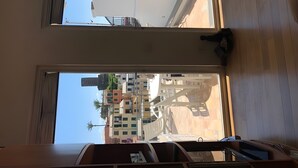 Una habitación con un ventanal grande, suelo de madera y vistas a un edificio de varios pisos con balcones.
