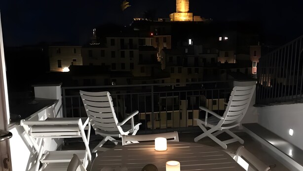 Una terraza en la azotea con una mesa redonda, sillas blancas y velas.