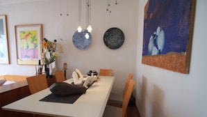 Un comedor con una mesa blanca, sillas de madera, un florero con flores y decoración en la pared.