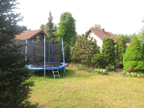 A backyard with a trampoline, a wooden playhouse, and a white house with a red roof. - Holiday Villa With a Garden, Close to the Lake (Stawiguda)
