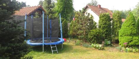 A trampoline in a backyard with a wooden fence, a ladder, and various trees and shrubs.