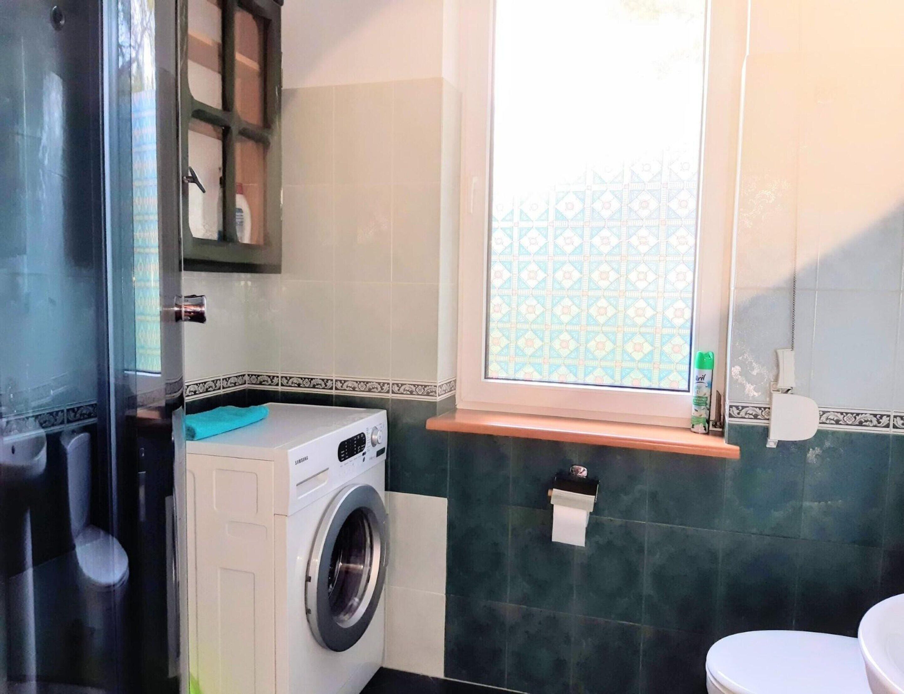 Un baño pequeño con lavadora, inodoro y una ventana con vidrio decorado.