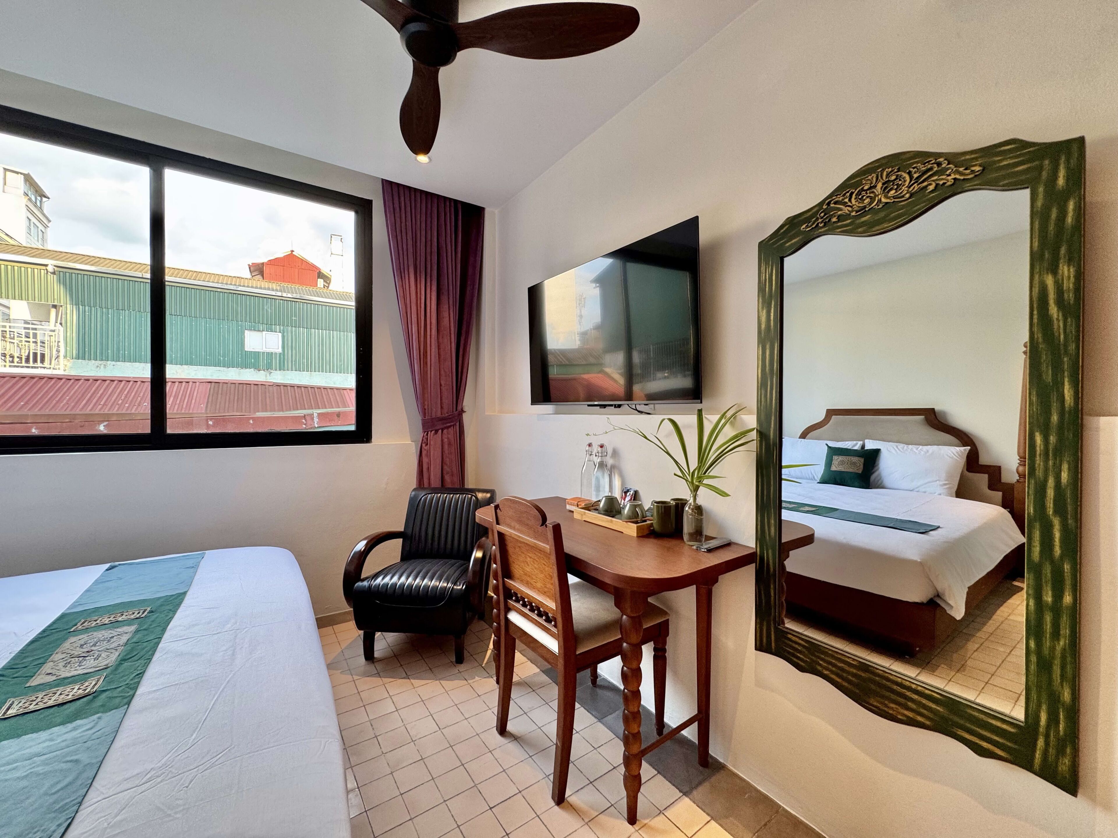 Quarto de hotel com cama, escrivaninha, cadeira, televisão e um espelho grande.