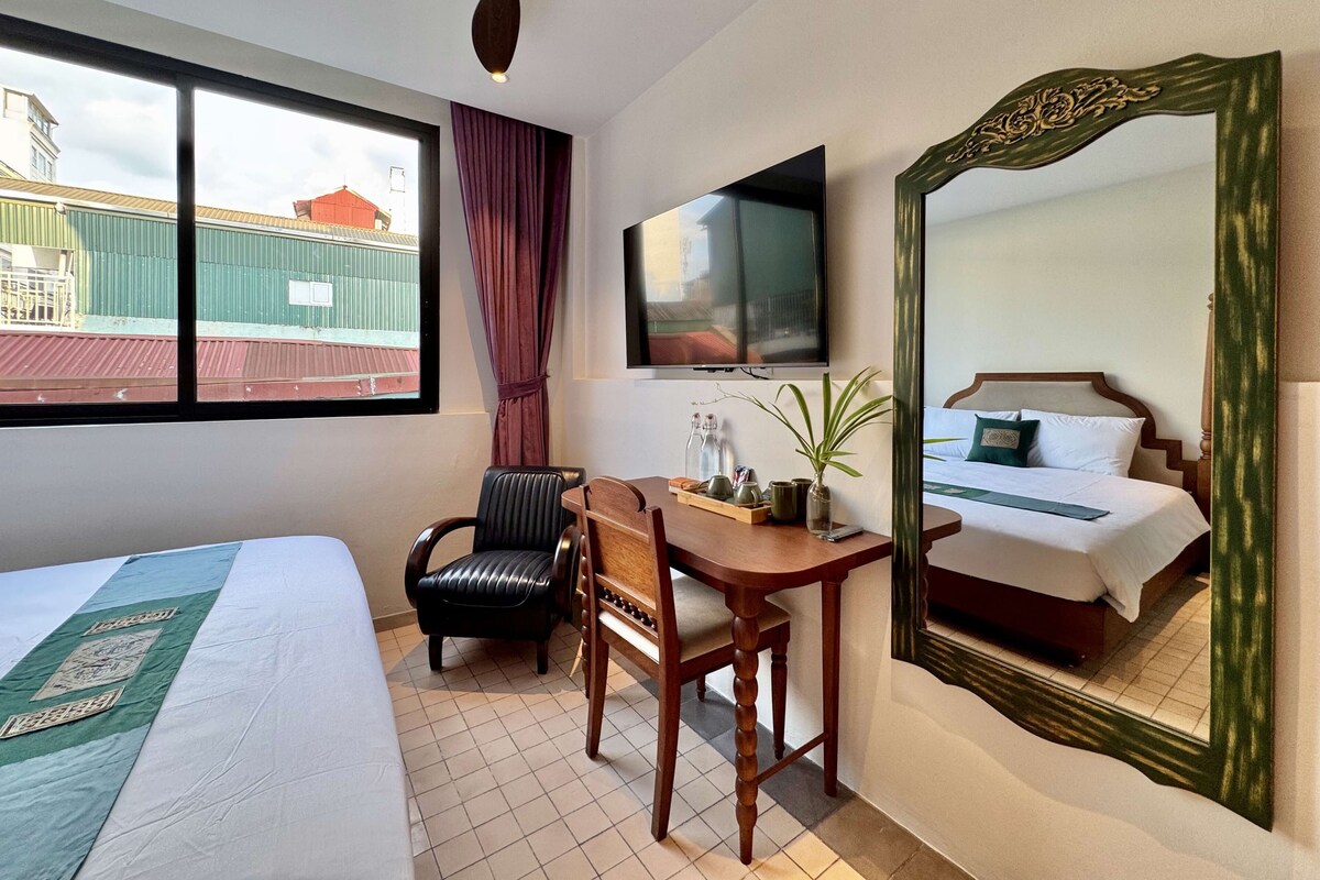 Ein Hotelzimmer mit Bett, Schreibtisch, Stuhl, Fernseher und einem großen Spiegel.