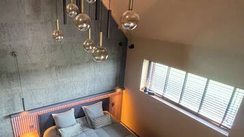 Un dormitorio moderno con techo inclinado, una cama grande, mesitas de noche, una ventana con persianas y lámparas colgantes.