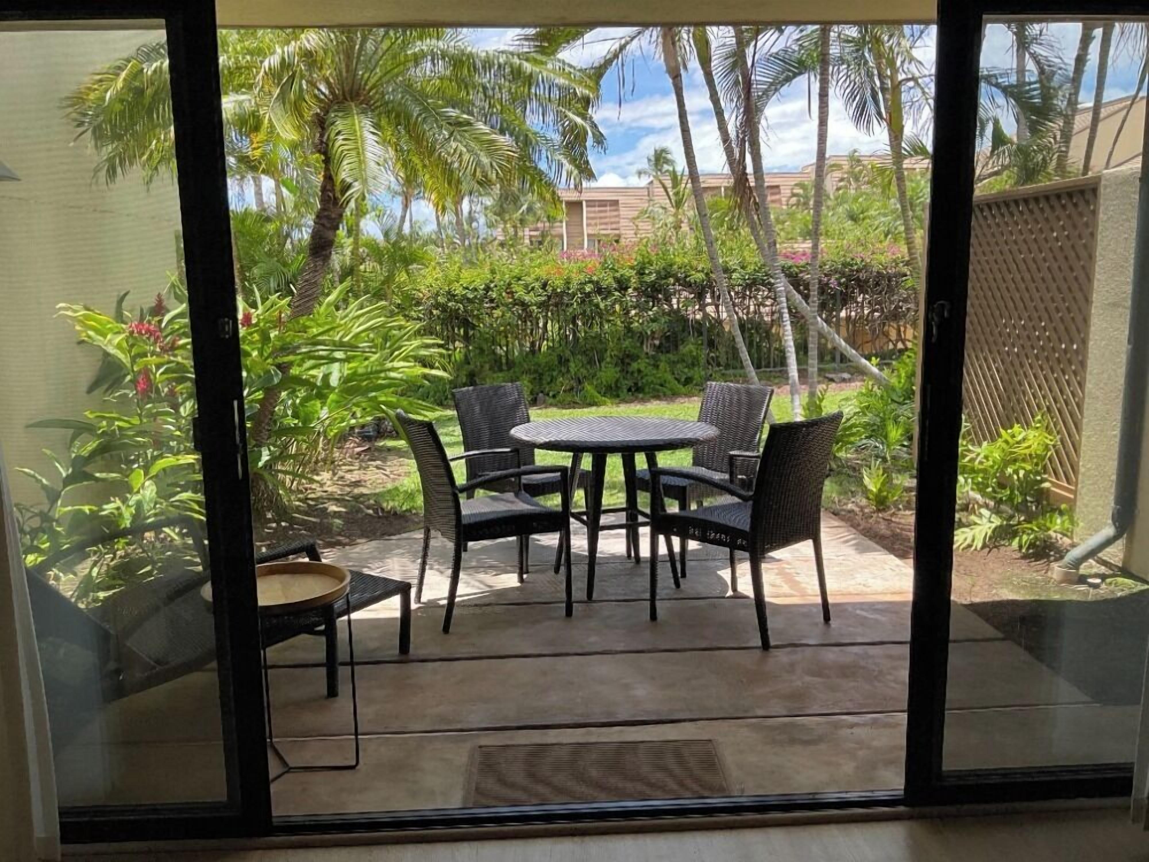 A patio with a round table and chairs, surrounded by lush greenery and palm trees.