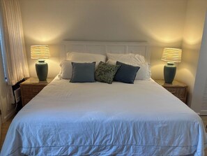 Una cama bien tendida con sábanas blancas y varias almohadas, flanqueada por dos mesitas de noche con lámparas.