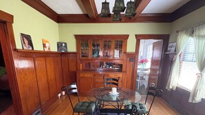 Una sala menjador amb una taula rodona, cadires, un penjoll, armaris de fusta i una finestra amb cortines.