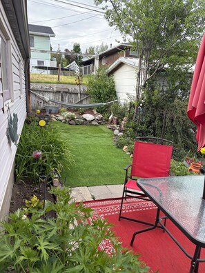 Ein Garten mit einem roten Stuhl, einem Glastisch und ein paar Blumen.