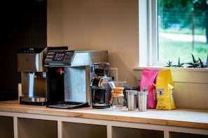 A coffee machine, a glass carafe, metal containers, and coffee bags on a wooden counter.