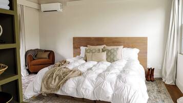 A bedroom with a wooden headboard, white bedding, a brown armchair, and a small shelf with a basket.