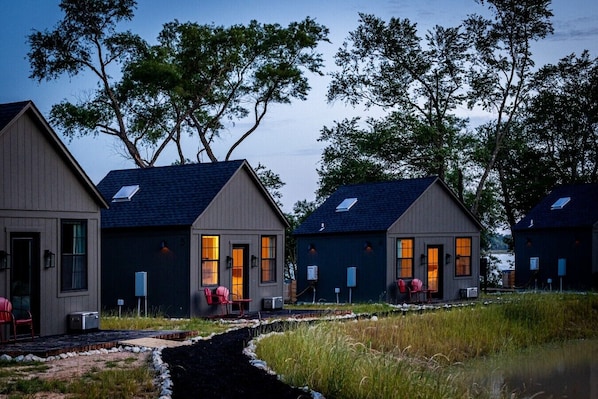 A row of cabins with a pathway leading to them, surrounded by trees and a body of water.